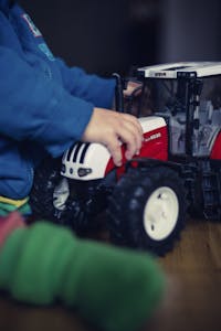 Person in Blue Jacket Holding Red and White Tractor Toy