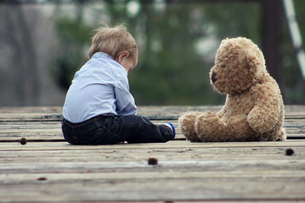 Boy Sitting With Brown Bear Plush Toy on Selective Focus Photo